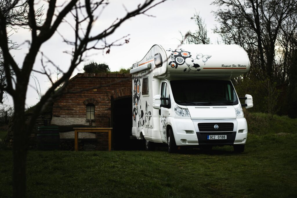 A white Fiat camper parked near a rustic brick shed in a rural landscape.